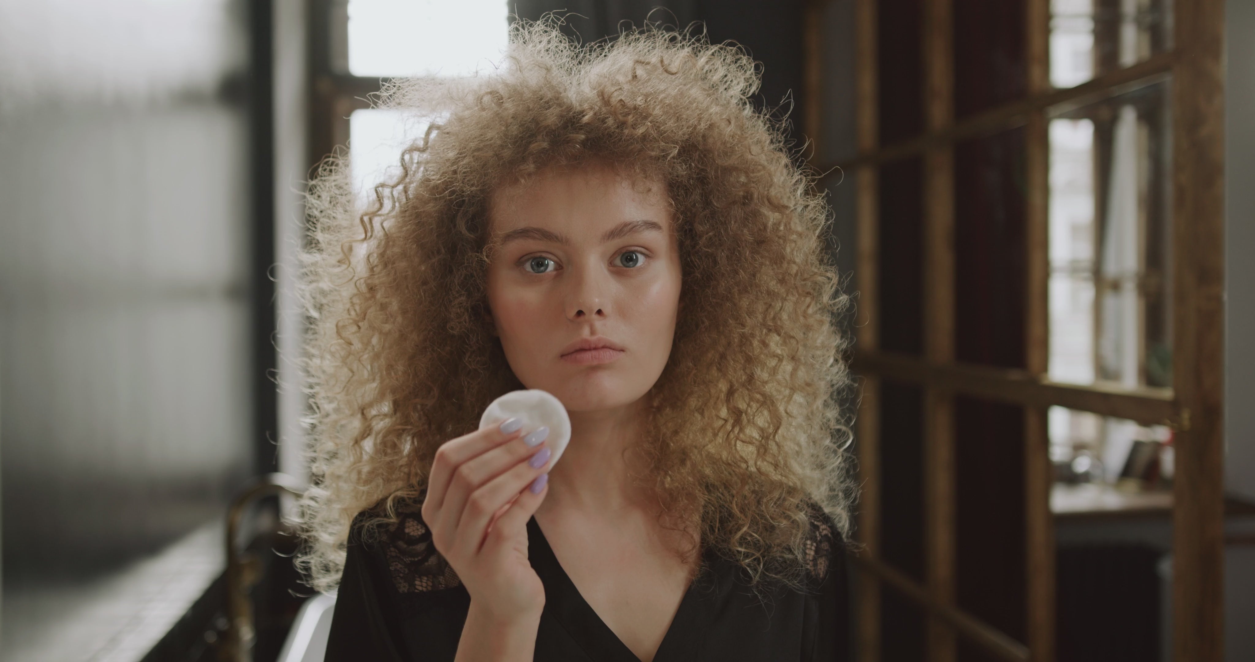 Ragazza riccia che applica il tonico viso con un dischetto di cotone durante la skincare, per una pelle idratata ed elastica